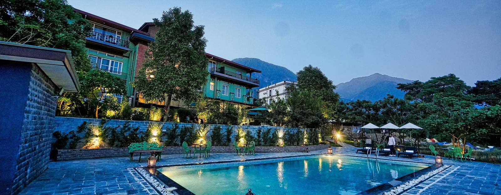 A picture with luxurious swimming pool, beautifully lit around and a scenic mountain view in the background - Atman, Dharamshala
