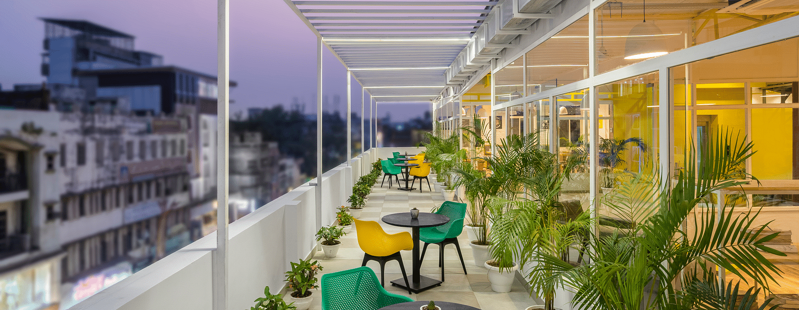 An image of a rooftop outdoor seating area featuring multiple chairs and tables, captured in the evening with lights illuminated.