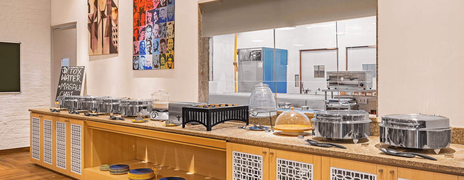 An interior side angle of buffet counter with numerous utensils on the shelves and wooden flooring.
