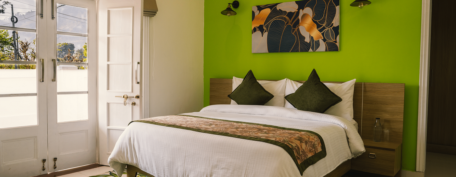A spacious room at BluSalzz Villas - The Green Roof, Bhimtal featuring a large bed, a photo frame above the headboard, a carpet, and a door leading to the balcony.