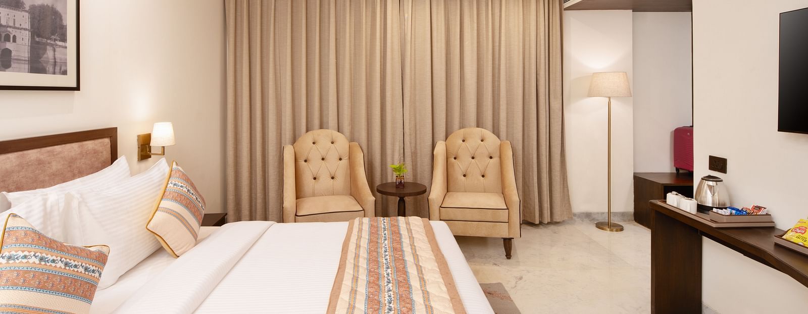 An image of a bedroom with double size, a photo frame hanged on the wall, two  chairs at one corner and opposite the bed there is a flat TV screen -  Brij Eternity, Vrindavan