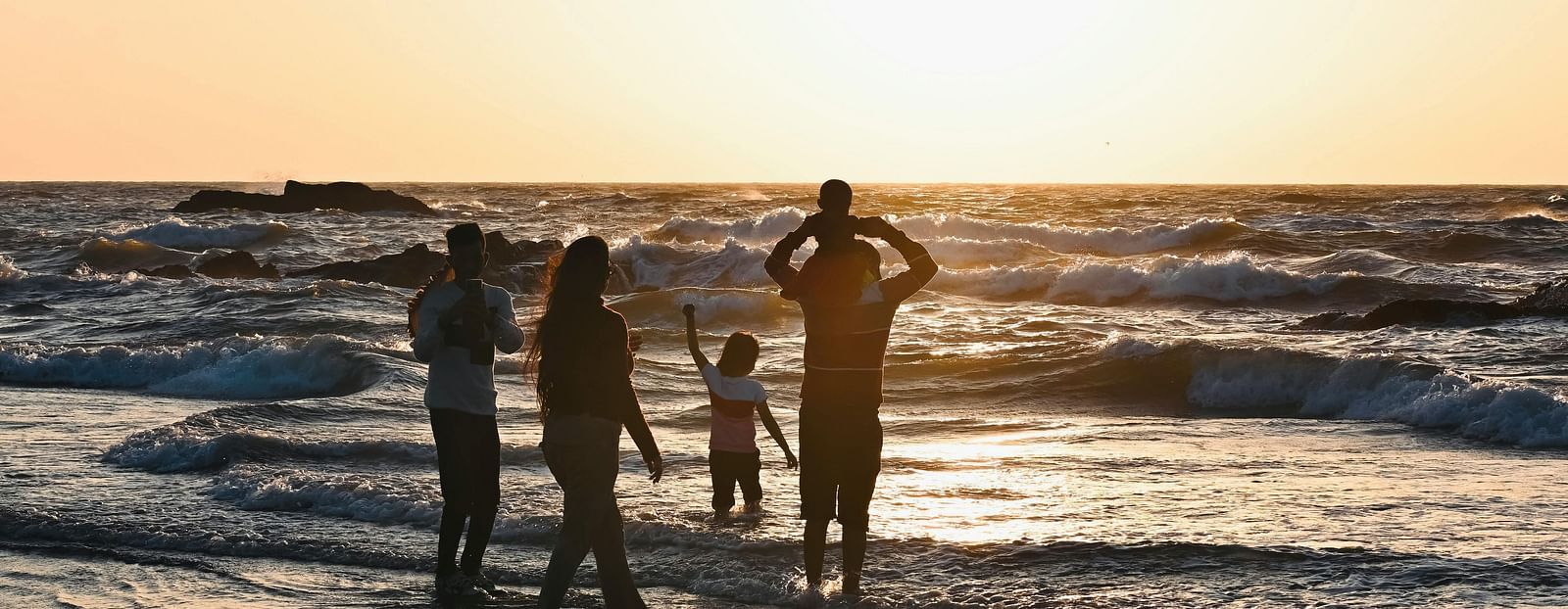 A family of five playing on a beach with the sun setting in the background.
