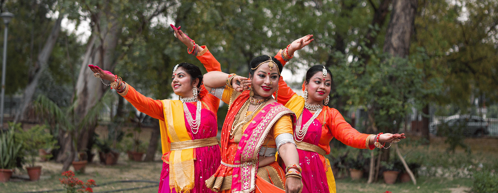 image of three women engaged in an Indian classical dance form with a lush green background in the surroundings