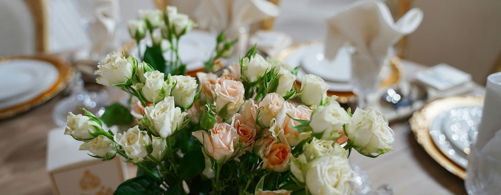 image of a vase with a lot of white and pink roses in the middle of a table that is set for an event or a banquet