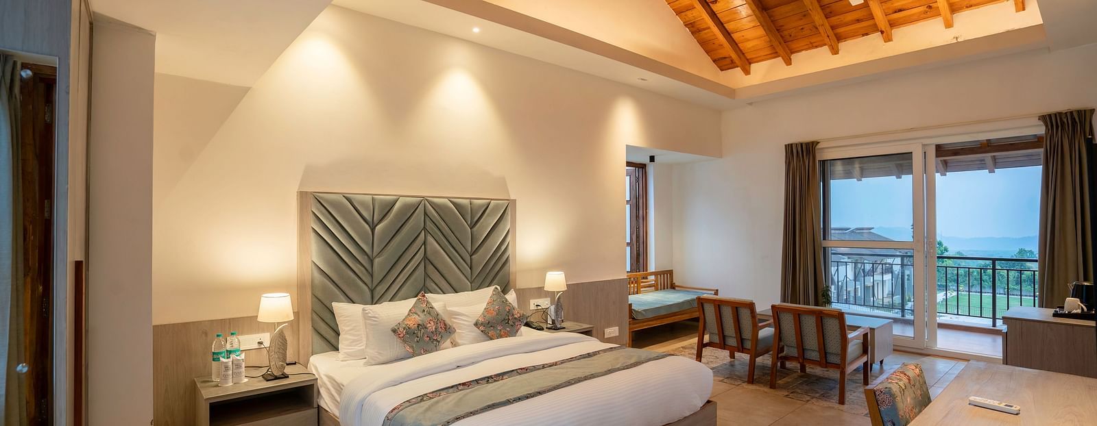 A modern hotel room with a king size bed, a seating area, and a view of the lush green outdoors.