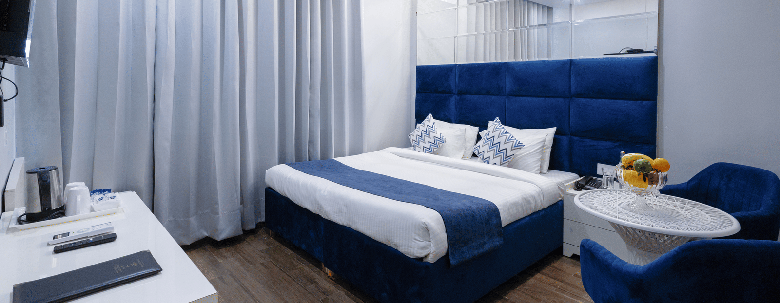 Deluxe Room featuring a bed with a blue headboard and white and blue linens, two blue chairs with a small round table, and light wood-look flooring. - Hotel Downtown17, Chandigarh