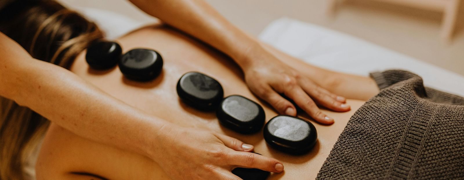 A therapist performing a hot stone massage on a patient's back, gently placing the heated stones along the spine.