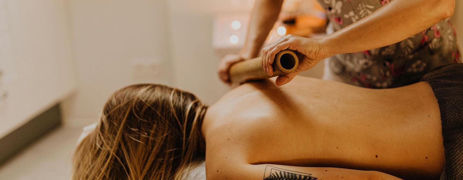 A therapist using a bamboo roller on a woman's shoulder.