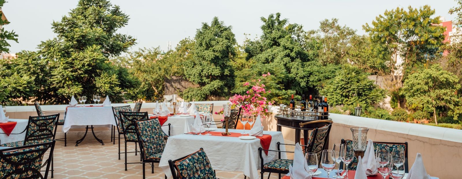 An outdoor dining terrace at Royal Heritage Haveli with tables set, overlooking trees and a distant landscape.