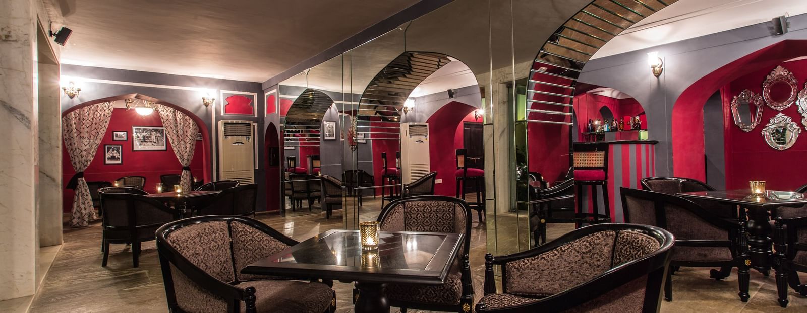 Interior view of a restaurant or bar area at Royal Heritage Haveli with red accents, arched doorways, and wooden tables and chairs.