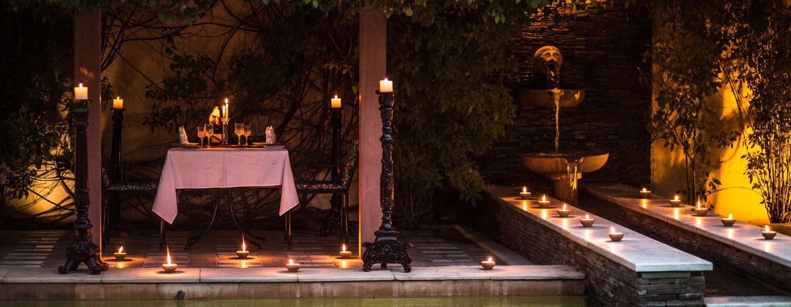 View of the outdoor setup with candles and a table next to water, similar to the first image, at Royal Heritage Haveli.