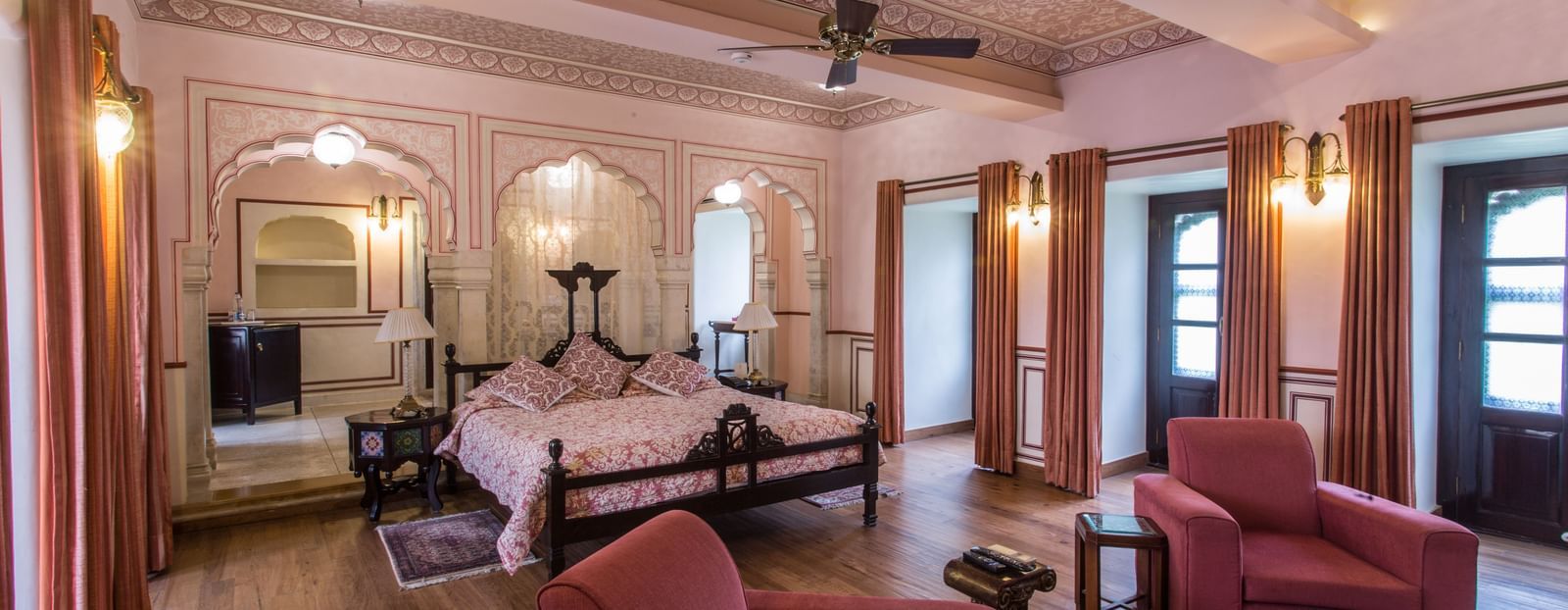 A spacious living area of a suite at Royal Heritage Haveli with traditional furniture, a ceiling fan, and light-coloured walls.