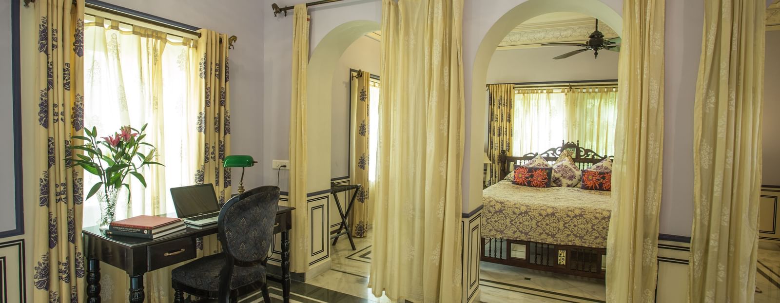 A room at Royal Heritage Haveli with a desk area in the foreground and a view into a connected bedroom through an archway.
