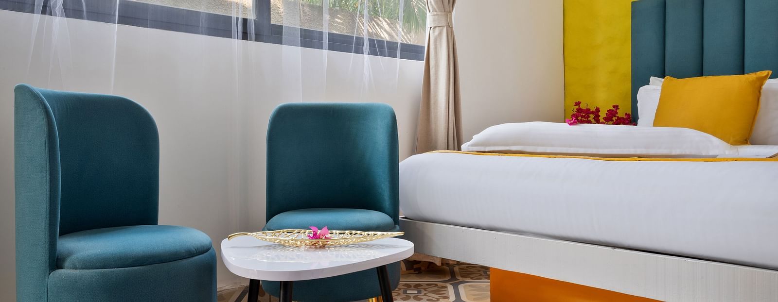 Room showcasing an airy space with a cosy seating area, teal chairs, and a glass table.