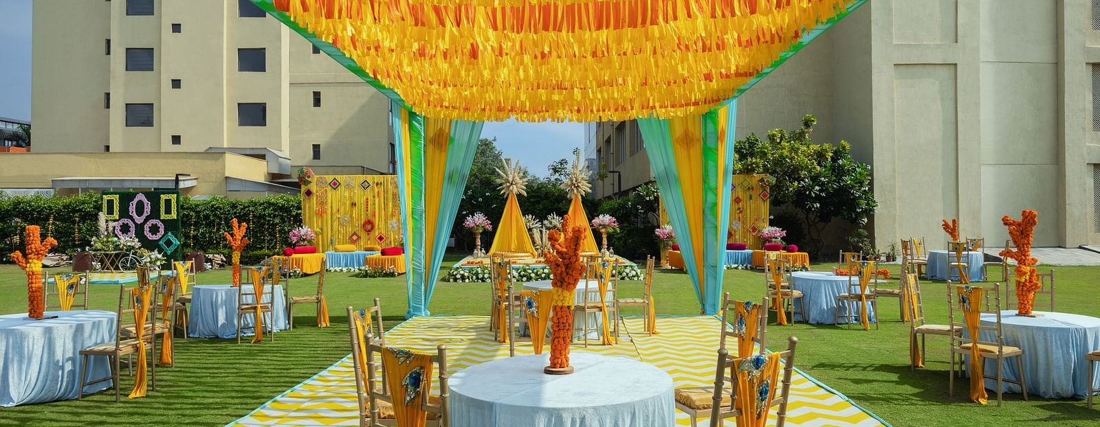 two tables with chairs in a cluster seated underneath a canopy during a sunny afternoon for shade - The Hideaway Banquets & Lawns, Greater Noida