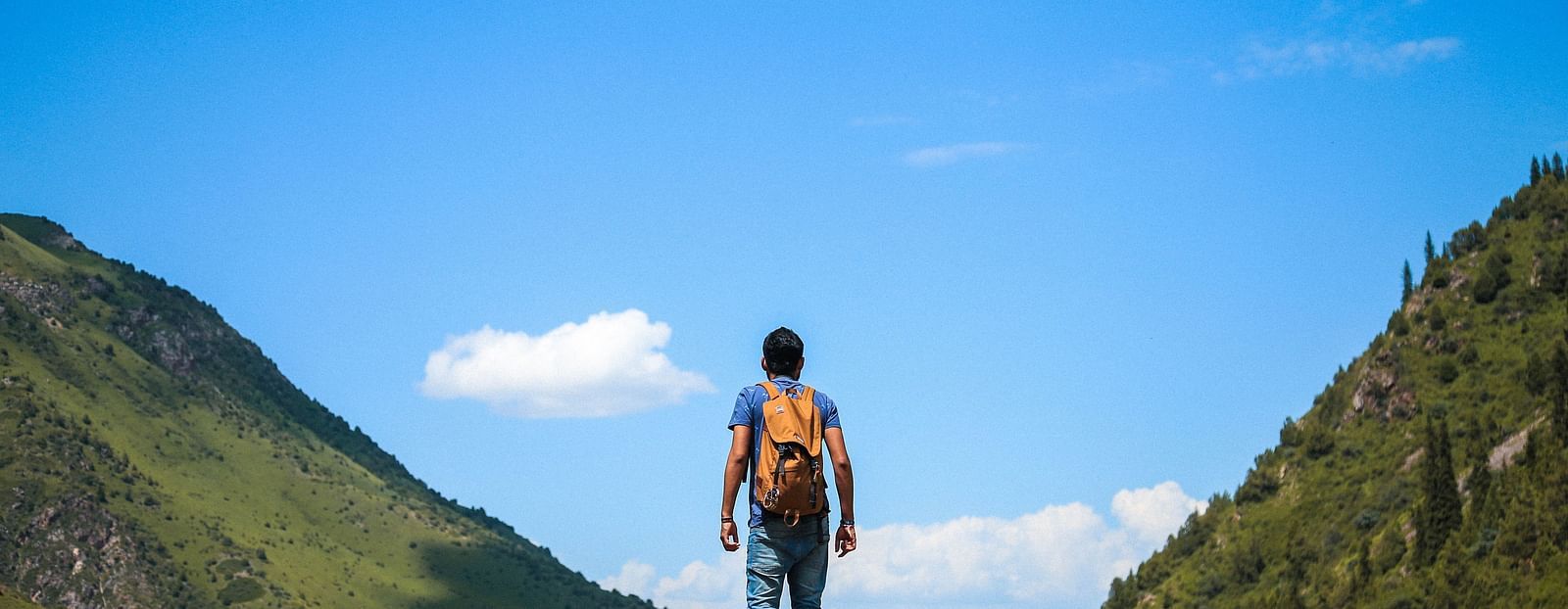 An image of a boy standing on a peak with a background of two hills and an open sky