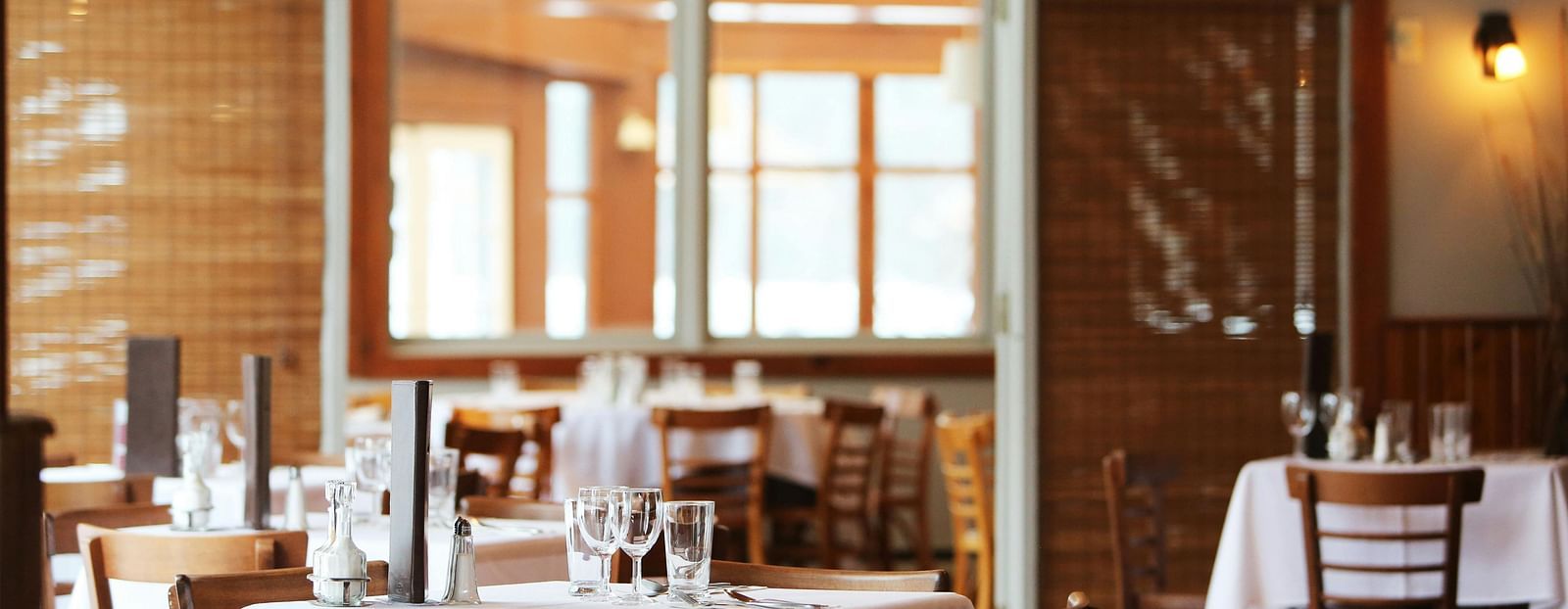 A neatly set up restaurant with wooden chairs around the tables.