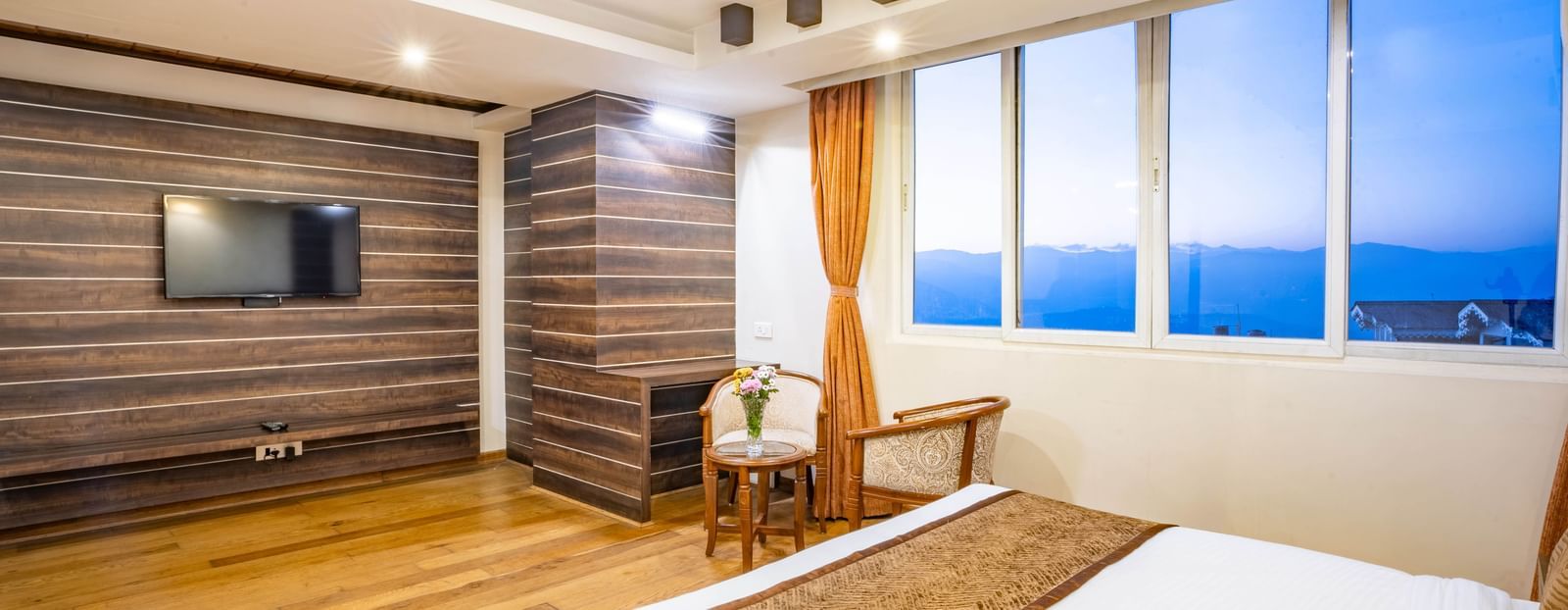 A spacious and well-lit hotel room with a large bed, seating area, and a flat-screen TV at the Yashshree Jai Hotel & Banquet, Darjeeling.