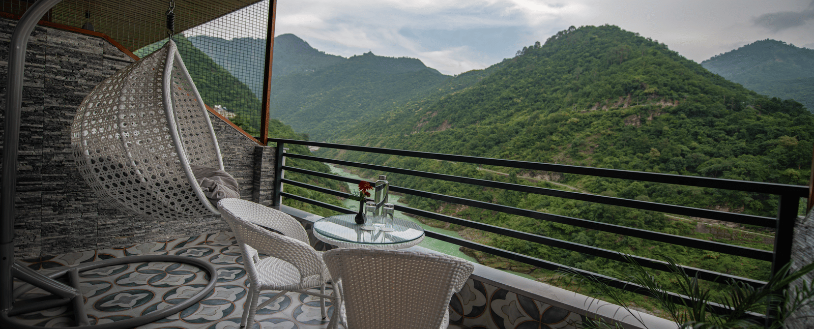 Balcony at The Tattva Devaprayag with two white chairs and a table overlooking the mountains and flowing river.