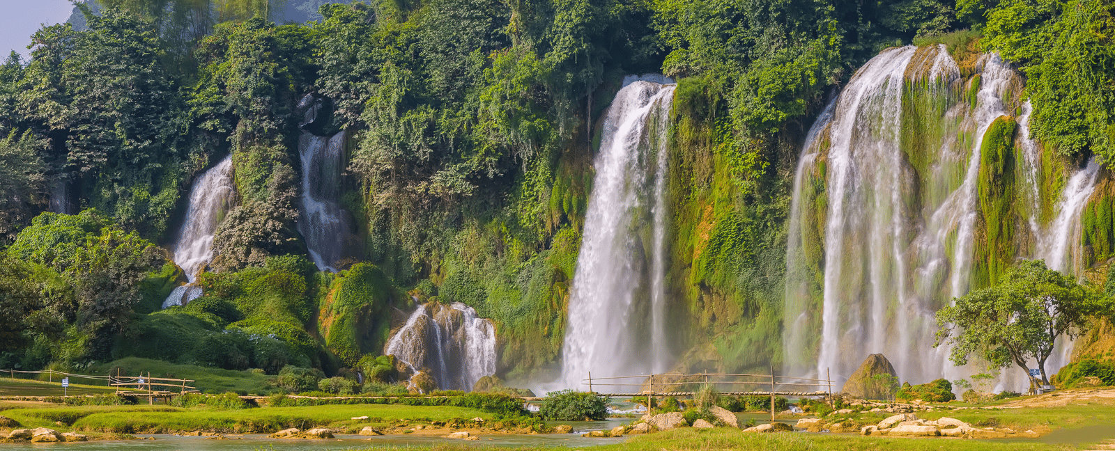 Cascades of waterfalls tumble down a lush cliff face into a wide river