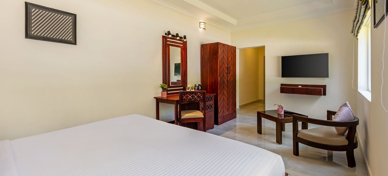 A well-lit hotel room with a bed, a desk, a wardrobe, a television, and a seating area - Mango Hill Resort, Coimbatore
