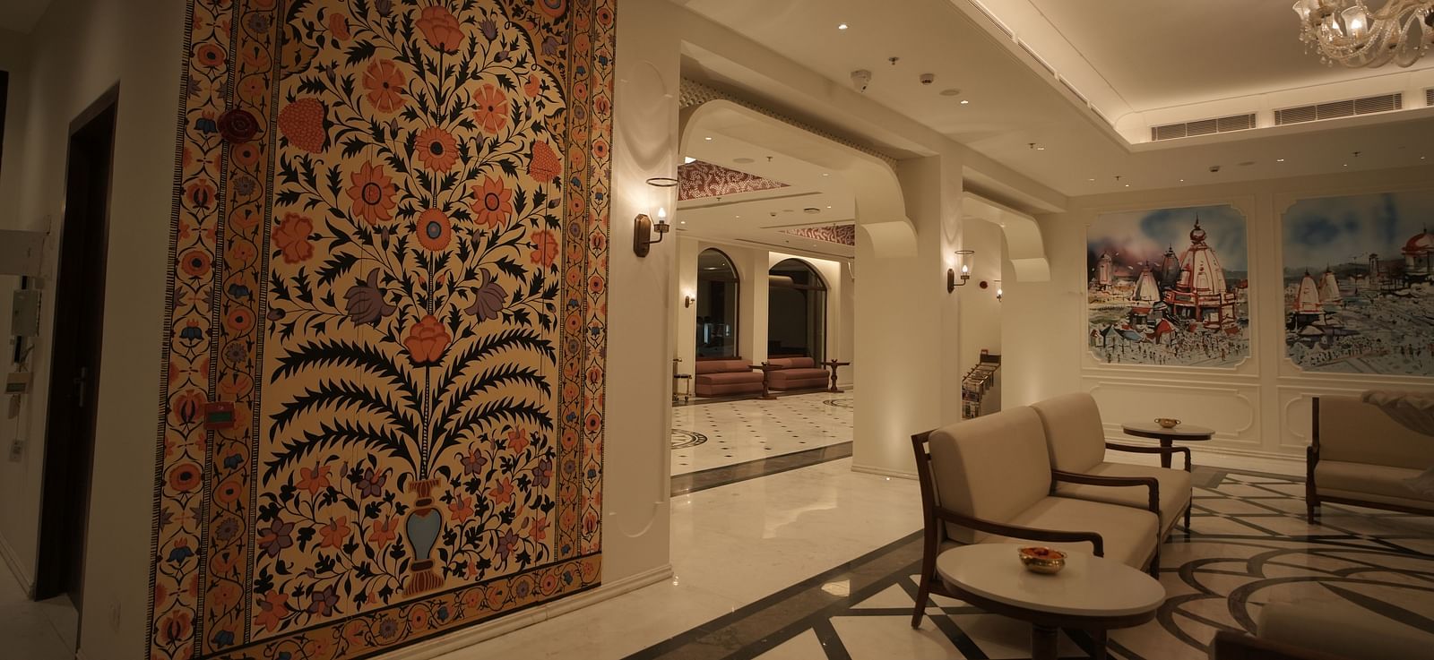 The reception area at Bhagirathi by RDB Atishay with warm lighting and intricate paintings on the walls.
