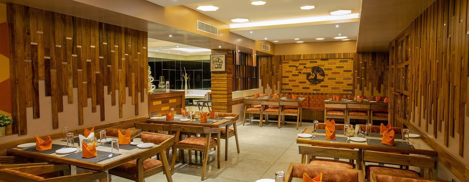 Image of Honeycomb Restaurant at Coral Reef Hotel & Spa in Port Blair showing dining setting of 4 chairs at each table and cutlery organised