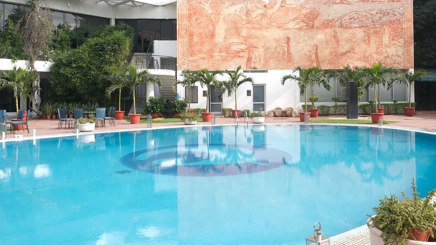 A large, bright blue swimming pool surrounded by lounge chairs and palm trees at Clarks Amer, Jaipur.