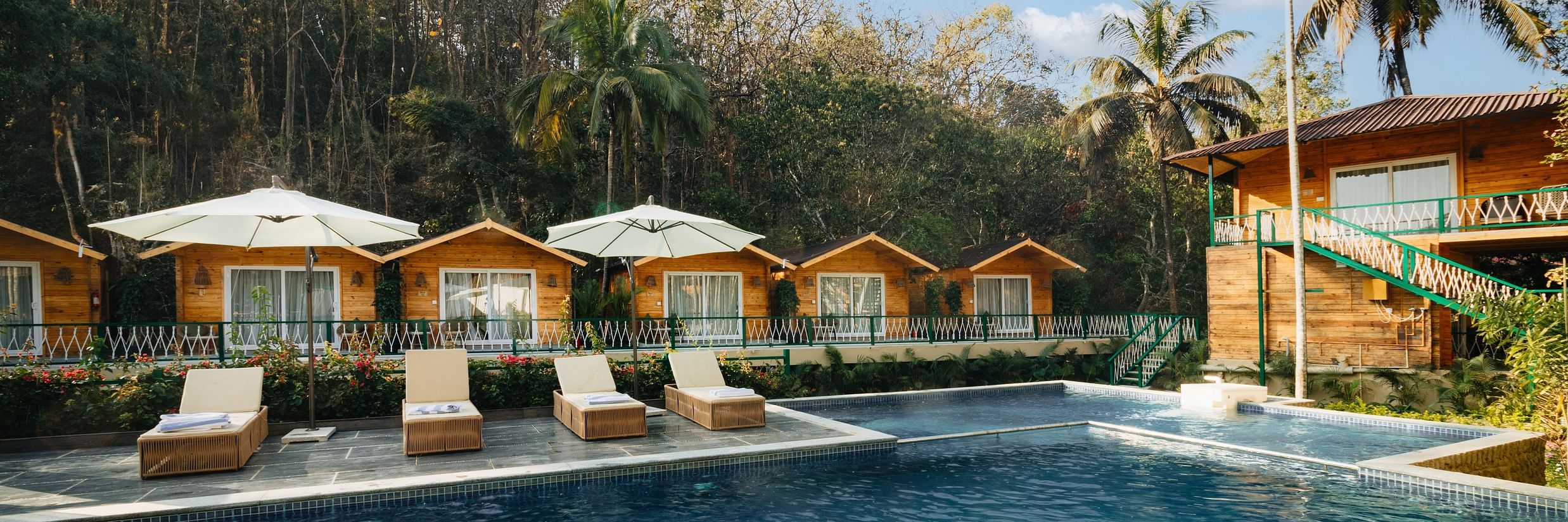 Row of cottages with loungers and a swimming pool in front of it - Stone Wood Jungle Resort, Dandeli