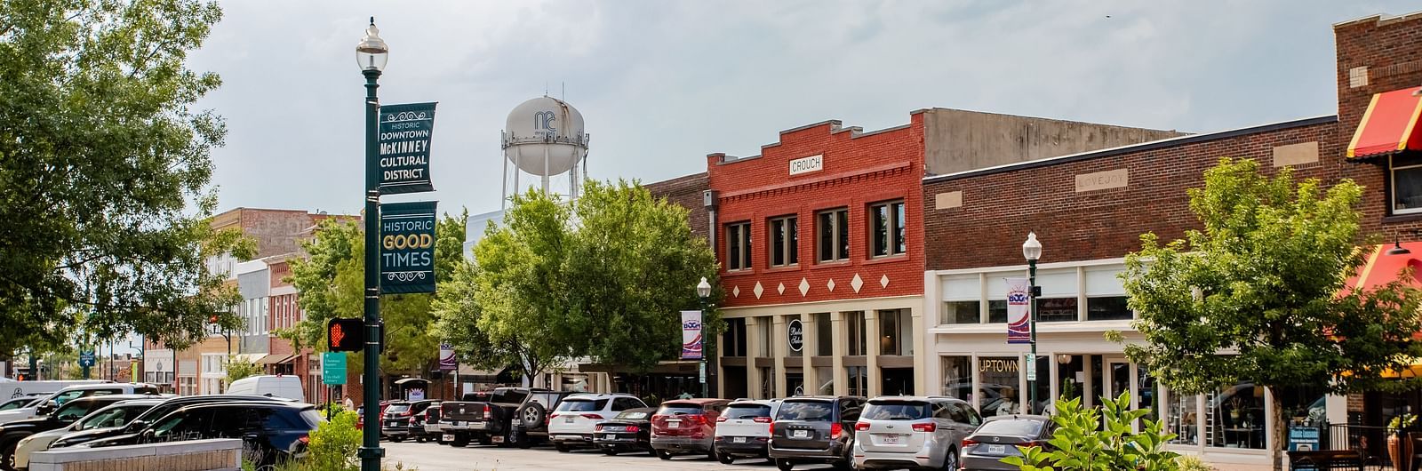 A town square with a welcome sign, a water tower in the background, and small businesses along the street.- The Grand Hotel & Ballroom, McKinney