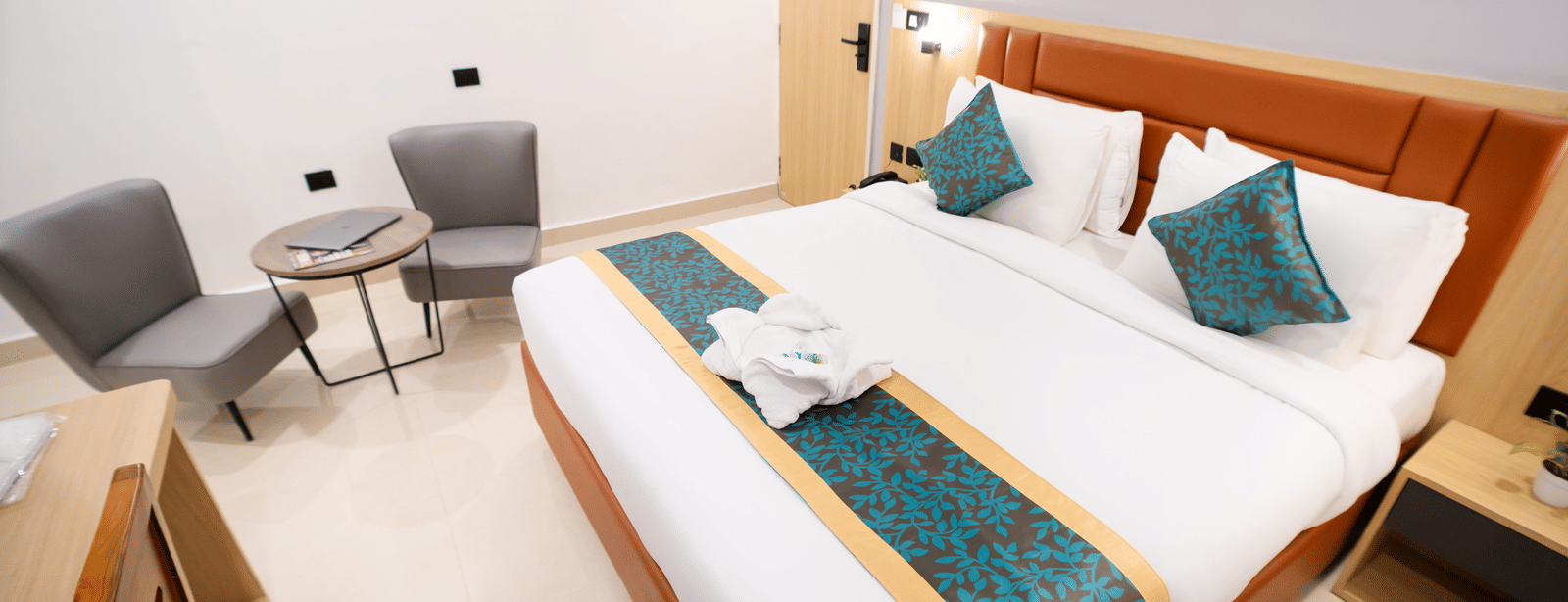 View of a spacious room with a large bed with a headboard, bedside tables on both sides, and a seating area to the side at Sunrise Business Hotel, Hyderabad.
