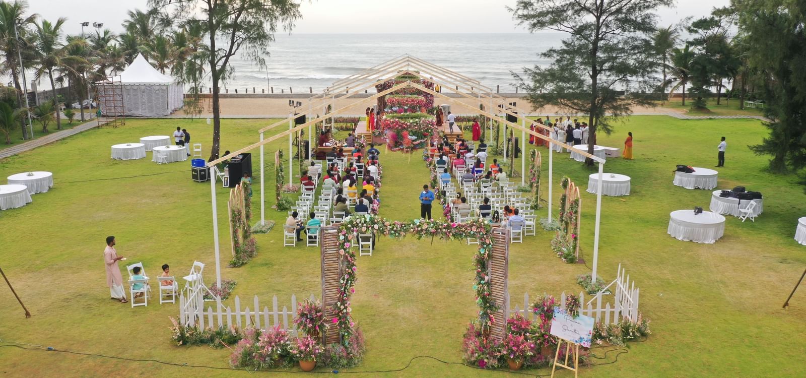 An outdoor event setup on a green lawn with a decorative archway, tables, and chairs, and palm trees under a bright sky | Horizon | Grand Bay Resort and Spa