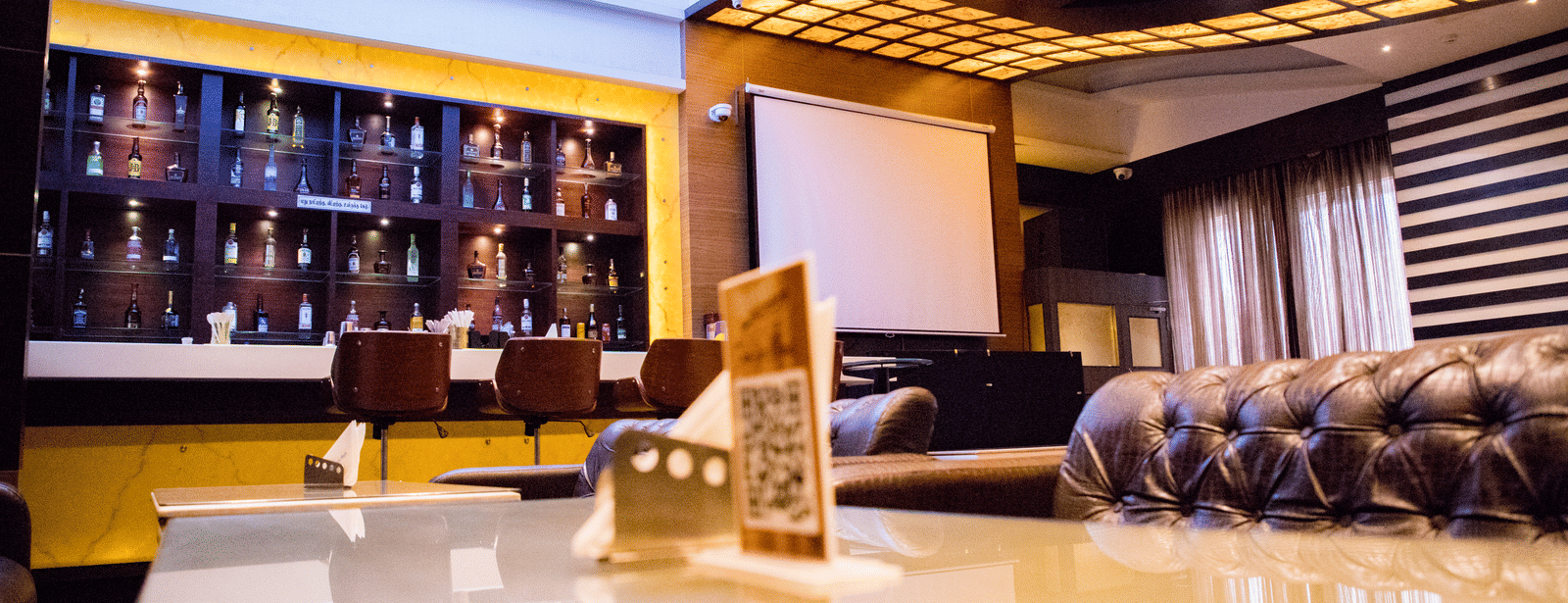 The bar at the Benzz Park, Vellore, taken from the dining table in the restaurant showcasing various liquor bottles on display behind the bar counter.