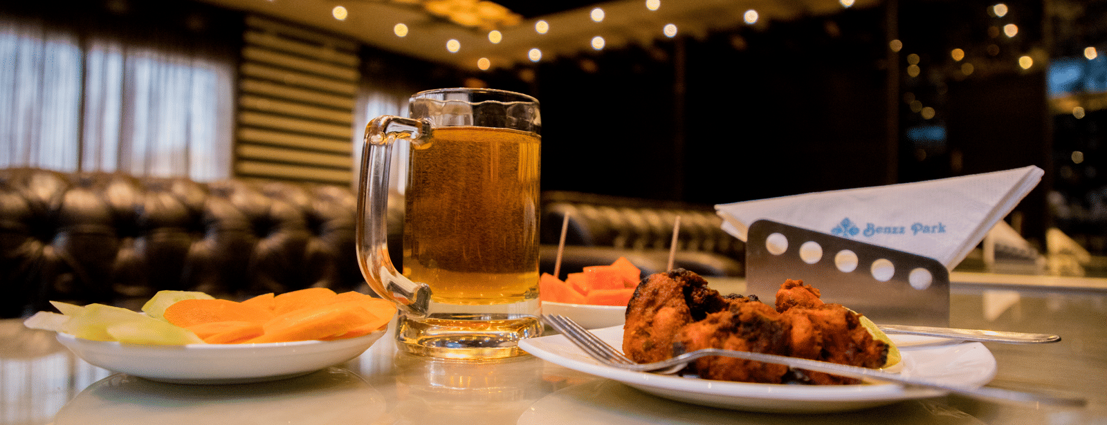 A close up shot of delicious side dish served with a plate of salad and a pint of beer on a dining table at Benzz Park, Vellore.