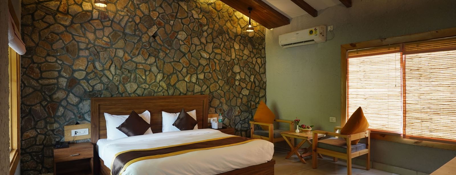 Luxury bedroom with stone accent wall, modern lighting, and double bed at Corbett Nirvana Resort.