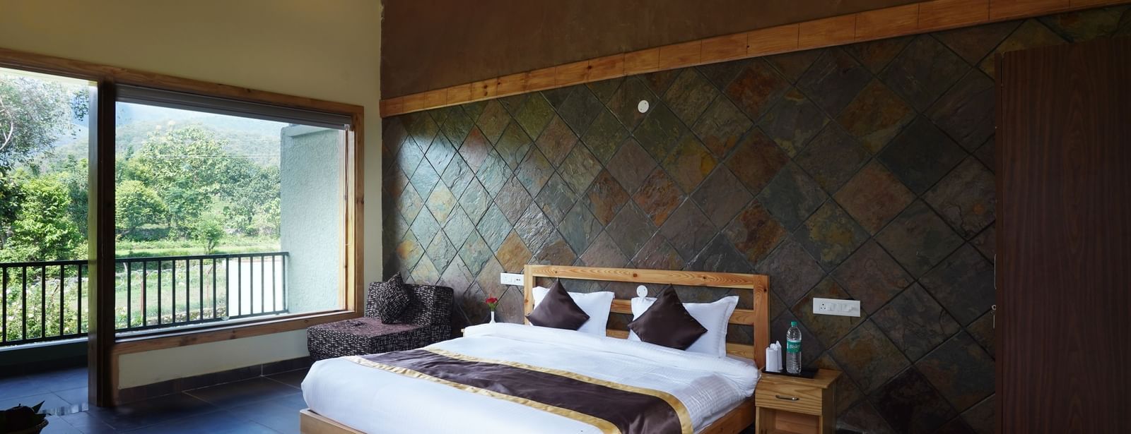 Premium resort room with stone wall accents and scenic outdoor views at Corbett Nirvana Resort.