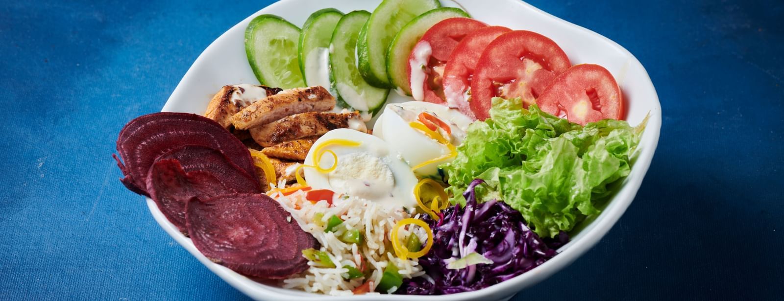 A bowl of fresh salad with sliced cucumber, tomato, beetroot, lettuce, and dressing at Grande Bay Resort & Spa.