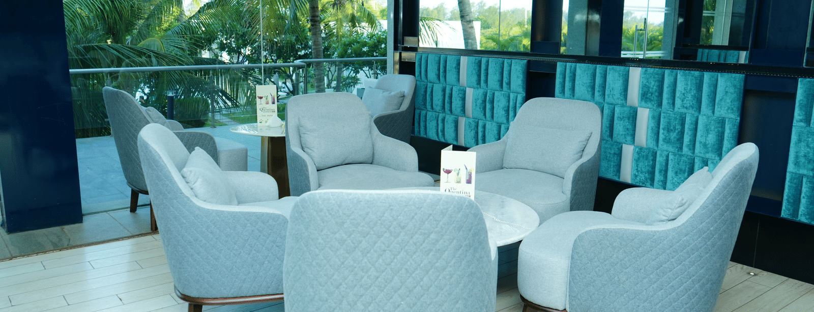 Cosy seating clusters inside The Quentina Bar featuring plush grey chairs and coconut tree views through large windows - Grande Bay Resort & Spa, Mamallapuram