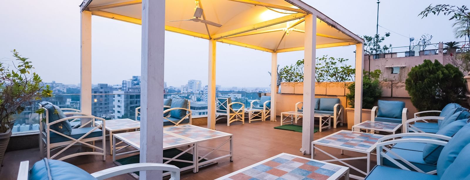 An outdoor dining setup at Hotel Ashok Nagpur featuring cushioned chairs and tables arranged on a rooftop or terrace during the evening.