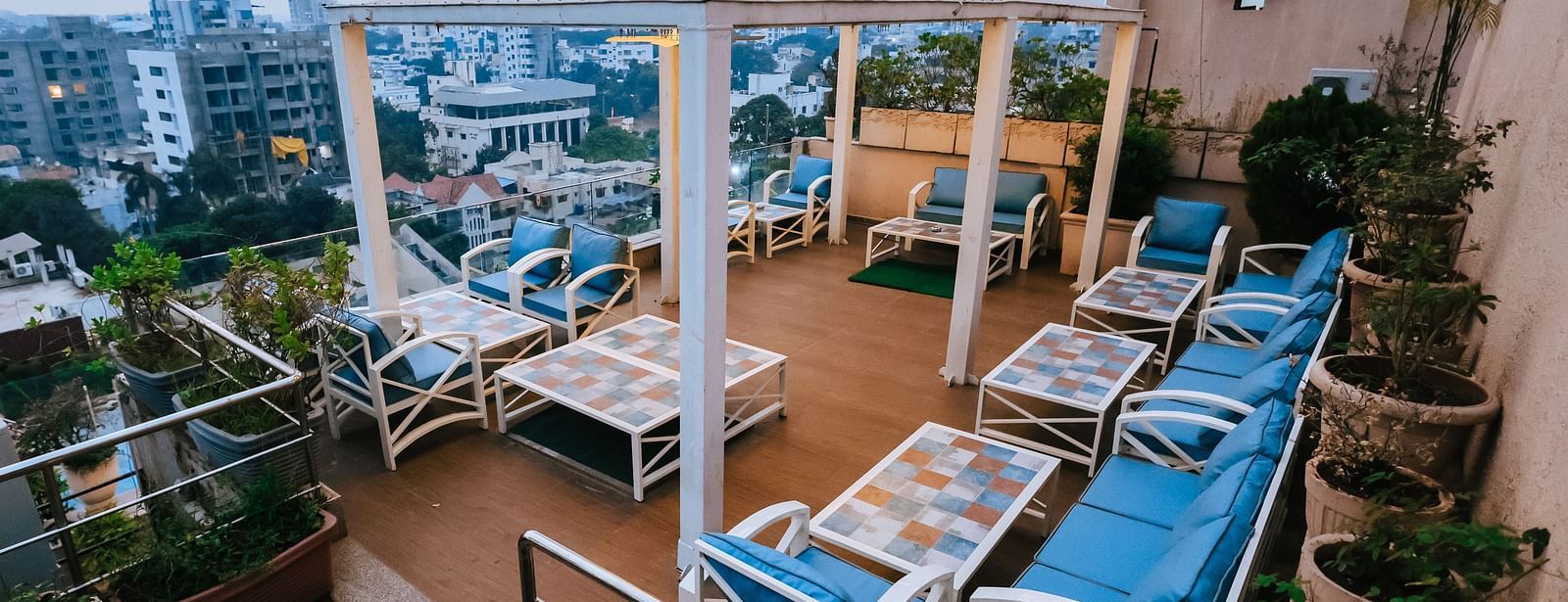 An outdoor dining setup at Hotel Ashok Nagpur featuring blue cushioned lounge chairs, potted plants, and a partially visible white canopy.