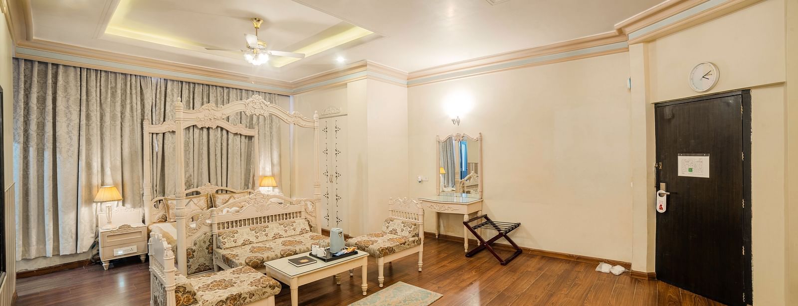 King Suite featuring a bed and a seating area with sofas and a coffee table, a wooden floor, and a door.- Hotel Ashok Nagpur
