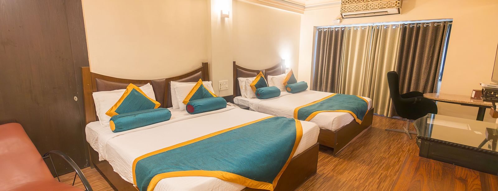Family Room featuring two beds, a chair, and wooden flooring.- Hotel Ashok Nagpur