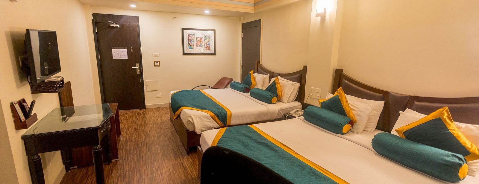 Family Room featuring two beds with white linens, teal and yellow accents, and dark wood headboards. - Hotel Ashok Nagpur