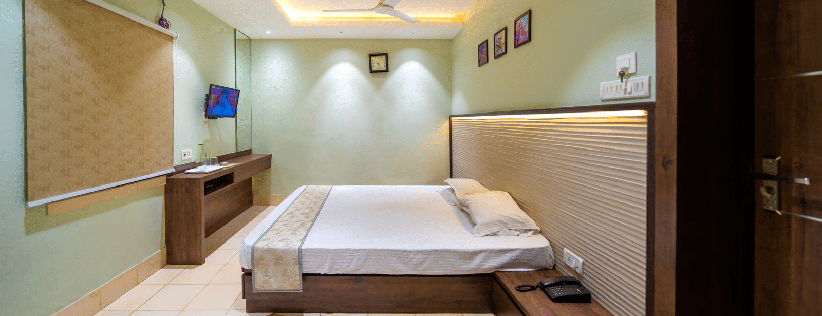 Minimalist bedroom with a double bed, ceiling lights, wall-mounted TV, and light-coloured walls – Hotel Dolphin Puri