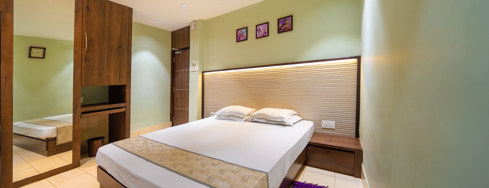 Minimalist room with double bed, wooden furniture, ceiling fan, and framed artworks above the bed – Hotel Dolphin Puri