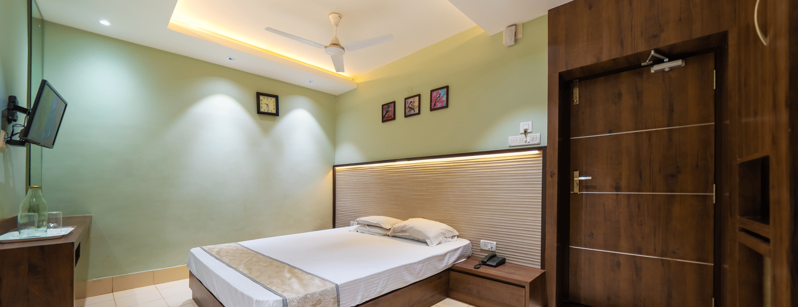 A modern hotel room with dark wood accents on the walls, a double bed, and a wall-mounted TV - Hotel Dolphin Puri