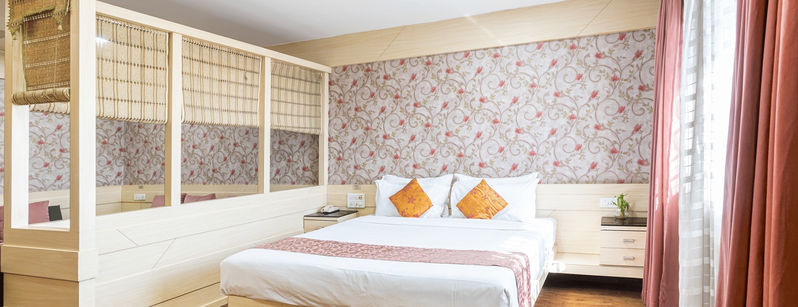 A room with white king size bed, floral wallpaper and wooden partition at Infiniti Hotel, Indore.