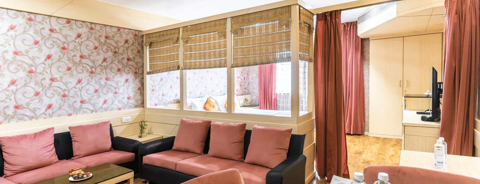 A lounge area with sofas, red chairs, wallpapered wall and wooden table at Infiniti Hotel, Indore.