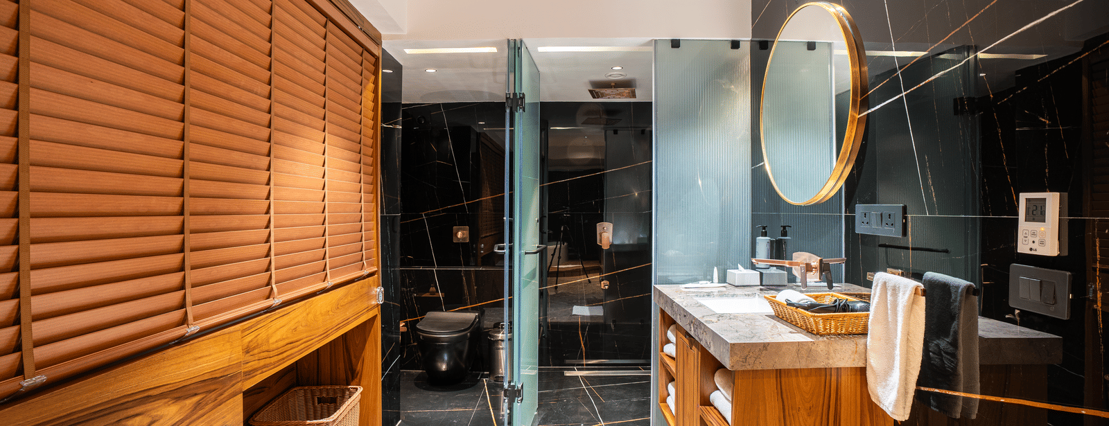 A bathroom with a wall mounted mirror, washbasin and glass shower partition at Infiniti Hotel, Indore.