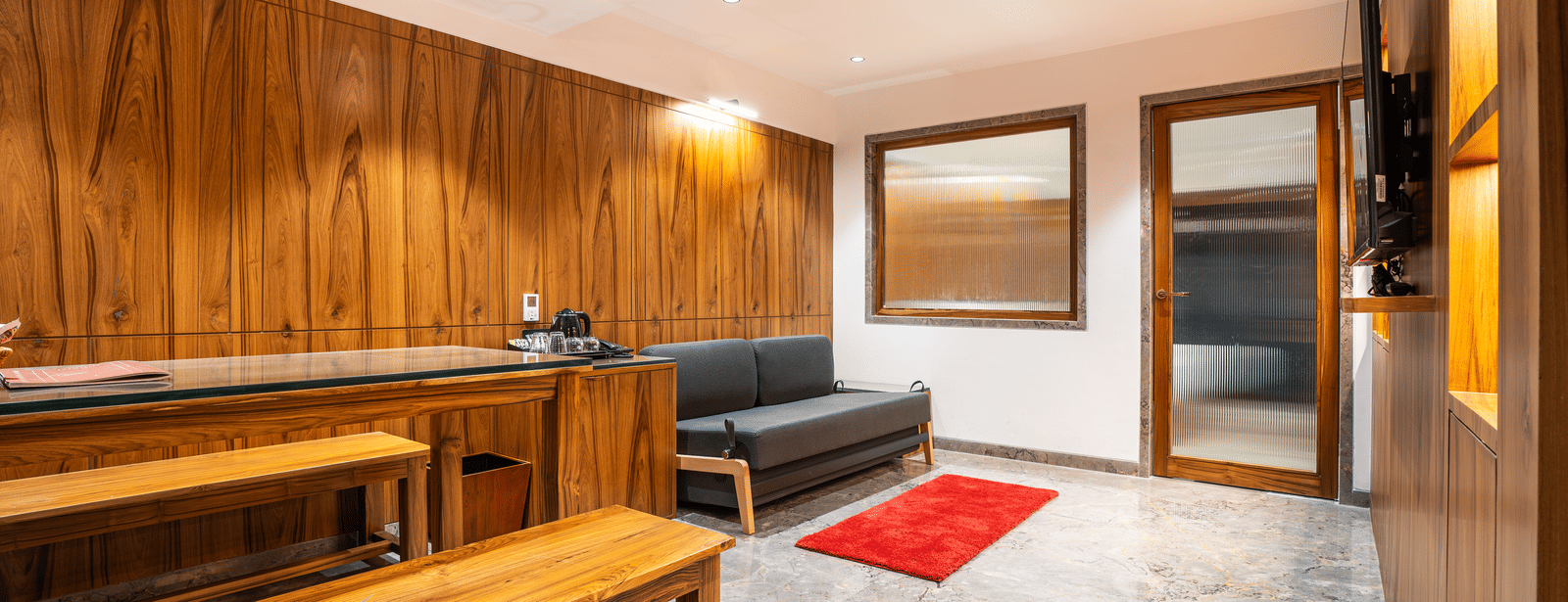 A suite with wooden interiors, long dining table, cushioned seating and red rugs at Infiniti Hotel, Indore.